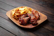Spicy BBQ chicken wings with sesame seeds and potato chips on dark boards background. Menu for a pub