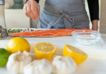 Wall Mural - Person seasoning a raw half salmon fillet with salt on a cutting board 