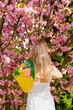 portrait of a blonde woman with a Japanese hat next to a blooming cherry tree.