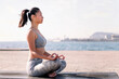 young asian woman in sportswear doing meditation by the sea on a yoga mat, concept of mental relaxation and healthy lifestyle, copy space for text