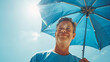 © Keitma - Happy man with sunny blue sky holding a blue umbrella or sunshade to protect his skin from sun light with return of warm days