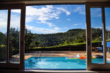 Fototapeta Londyn - Window View to a Beautiful Swimming Pool by the Mountains in the Countryside of Brazil