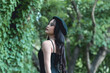 Young Asian woman in gothic outfit posing thoughtfully in forest