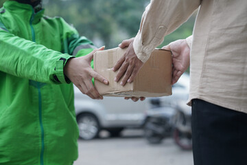 Online taxi driver motorbike wearing green jacket and helmet delivering package to customer