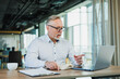 © Дмитрий Ткачук - An adult bearded man is sitting at a laptop and working in the office. A gray-haired man runs an online business.