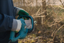 Close-up Of A Man Trimming Branches In A Garden With An Electric Hedge Trimmer
