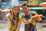 Fototapeta Panele - Happy traveler european man and woman wearing summer shirt holding colourful squirt water gun over blur city, Water festival holiday concept