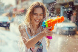 Fototapeta Panele - Happy traveler european woman wearing summer shirt holding colourful squirt water gun over blur sea, Water festival holiday concept
