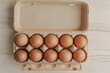 Ten organic brown eggs neatly placed in a recyclable paper carton, on a wooden table.