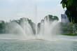High jets of water from a fountain in a lake, surrounded by lush greenery in an urban park, under a clear sky.