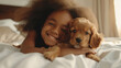 A little girl tenderly hugs her puppy and lies on the bed in a bright bedroom in the morning. Friendship concept between child and pet, copy space for text
