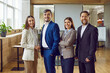 © Studio Romantic - Portrait of confident business people men and women wearing suit looking cheerful at camera and smiling standing in modern office. Company employees or group of staff in meeting room.