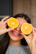 Happy female teenager with braces covering her eyes with an orange fruit.