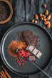 Schokolade, kakaopulver und rote Pfefferkörner auf einem schwarzen Teller. Backen, Zutaten, Draufsicht.