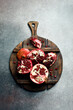 A wooden kitchen cutting board with a piece of fresh pomegranate. On a concrete background.