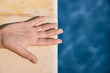© Amparo Garcia - Hand of an unrecognizable person is resting on a poolside ledge, the hand is wet, wrinkled and the ledge is made of stone