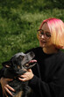 A young attractive woman with pink hair and glasses hugs with her Blue Heeler in spring park. Australian cattle dog on a walk with female owner. Family dog outdoor lifestyle concept.