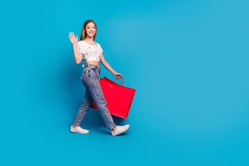 Sticker - Full size photo of nice young girl arm wave walk empty space wear top isolated on blue color background