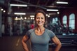 © Markus Schröder - Portrait of a merry woman in her 40s showing off a lightweight base layer over dynamic fitness gym background
