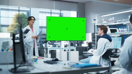 Leinwandbilder - Group of Students Listening to Their Young Biology Teacher Who Uses TV Monitor with Green Screen Template in a Laboratory. Team of Bioengineers Having a Meeting and Discussing Experiment Ideas