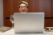 a girl with short hair and glasses indoors at a laptop laughs and smiles emotionally and cheerfully while working and chatting