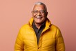 Portrait of a grinning indian man in his 60s donning a durable down jacket over pastel or soft colors background