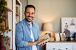 Portrait of a cheerful adult man holding a book for storytelling and leaning against a bookshelf.