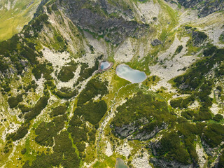 Aerial drone view above a glacier lagoon located in a rocky terrain, under mountain peaks. The ridges are populated by juniper bushes. Two lakes are shining through the ravines. Carpathia, Romania.