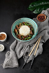 Poster - Asian food - boiled rice with fried beef and green beans in ceramic bowl on black stone background. Stir-fried beef with string beans and rice in modern style. Asian food menu in dark backdrop.