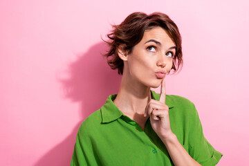 Poster - Photo of charming doubtful young woman dressed green shirt finger cheekbone looking empty space isolated pink color background