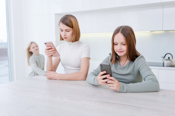 Two girls are sitting at table, both looking at their cell phones