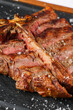 T-bone steak. Close up photo with a beef t-bone steak on a black platter with spread salt around it. Beef barbecue grill photo.
