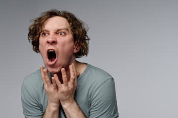 Wall Mural - Studio portrait of furious young Caucasian man with curly hair bawling, gray background, copy space