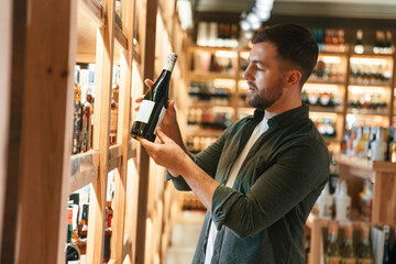 Wall Mural - Customer is looking at bottle. Man is choosing wine in the store