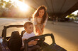 Mother having fun assisting toddler son while driving battery powered toy car