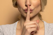 Closeup portrait of woman holding index finger on lips on beige background