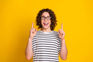 Sticker - Portrait of surprised nerd guy in striped t shirt fingers pointing up new favorite book at home library isolated on yellow color background