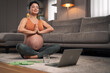 A contented pregnant woman meditating in the living room and doing yoga exercises