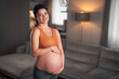 A portrait of a happy pregnant woman holding her belly and preparing to do yoga exercises at home