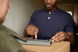 African man signing a digital tablet for a courier delivery