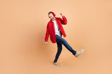 Wall Mural - Full length portrait of nice young man dancing listen music wear red shirt isolated on beige color background