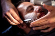 Barbershop. Barber shaving bearded male with a sharp razor.