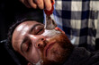 Professional hairdresser applying foam on customer's cheeks for shaving.