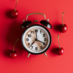 A creatively styled image of an old-fashioned alarm clock with cherries around on a vibrant red background