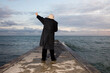 An unidentified man wearing a dark coat and hat standing on a pier trying to hail a taxi