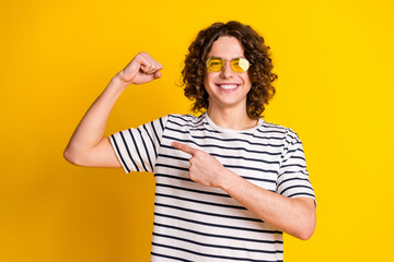 Sticker - Photo portrait of handsome teenager guy show muscle point biceps wear trendy striped garment isolated on yellow color background