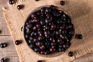 Wall Mural - Black currant in a bowl on wooden background. Organic berries. 
