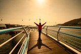 Fototapeta Na sufit - Traveler woman wear red clothes and raising arm standing on Songdo Skywalk at sunset in Busan, South Gyeongsang Province, South Korea.