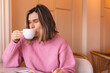 Thoughtful blonde woman drinking coffee in cafe, lifestyle, coffee, communication and local business, unaltered. Sensual woman with closed eyes. Girl wear pink sweater.