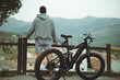© Taras Grebinets - Rear view young active man with electric bicycle standing on top of hill and contemplating a beautiful view of a city in the mountains on foggy day. Healthy lifestyle. Sport. Inspiration. Achievements